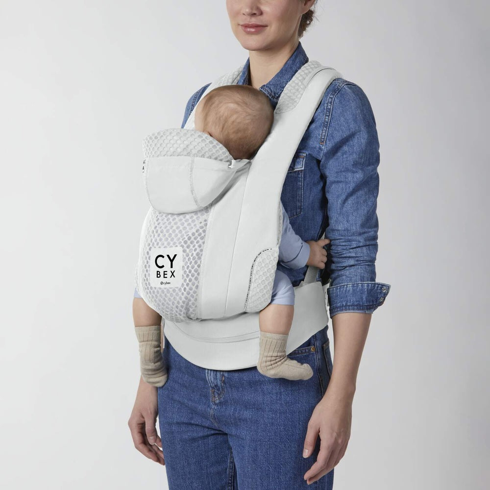 Close-up of the Cybex Coya Carrier in light gray with mesh panel, front-carried infant secured by adjustable straps; cybex logo visible.