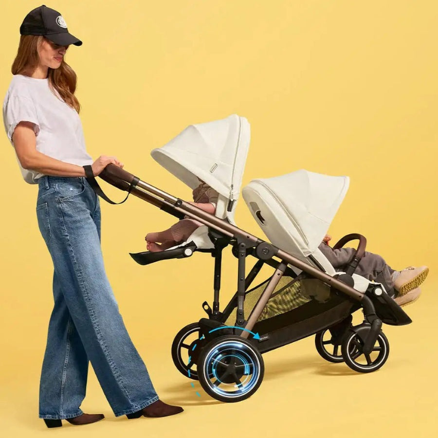 Close-up of the Cybex E-Gazelle S Stroller with twin white canopies, brown frame, blue-accent wheels being pushed by a woman.