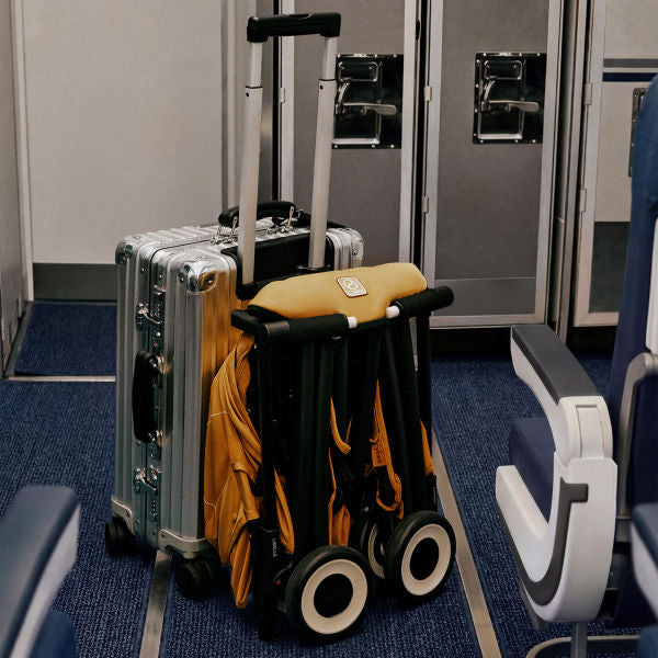 Cybex Libelle Ultra-compact Stroller in Cinnamon Yellow folded beside luggage at an airport gate