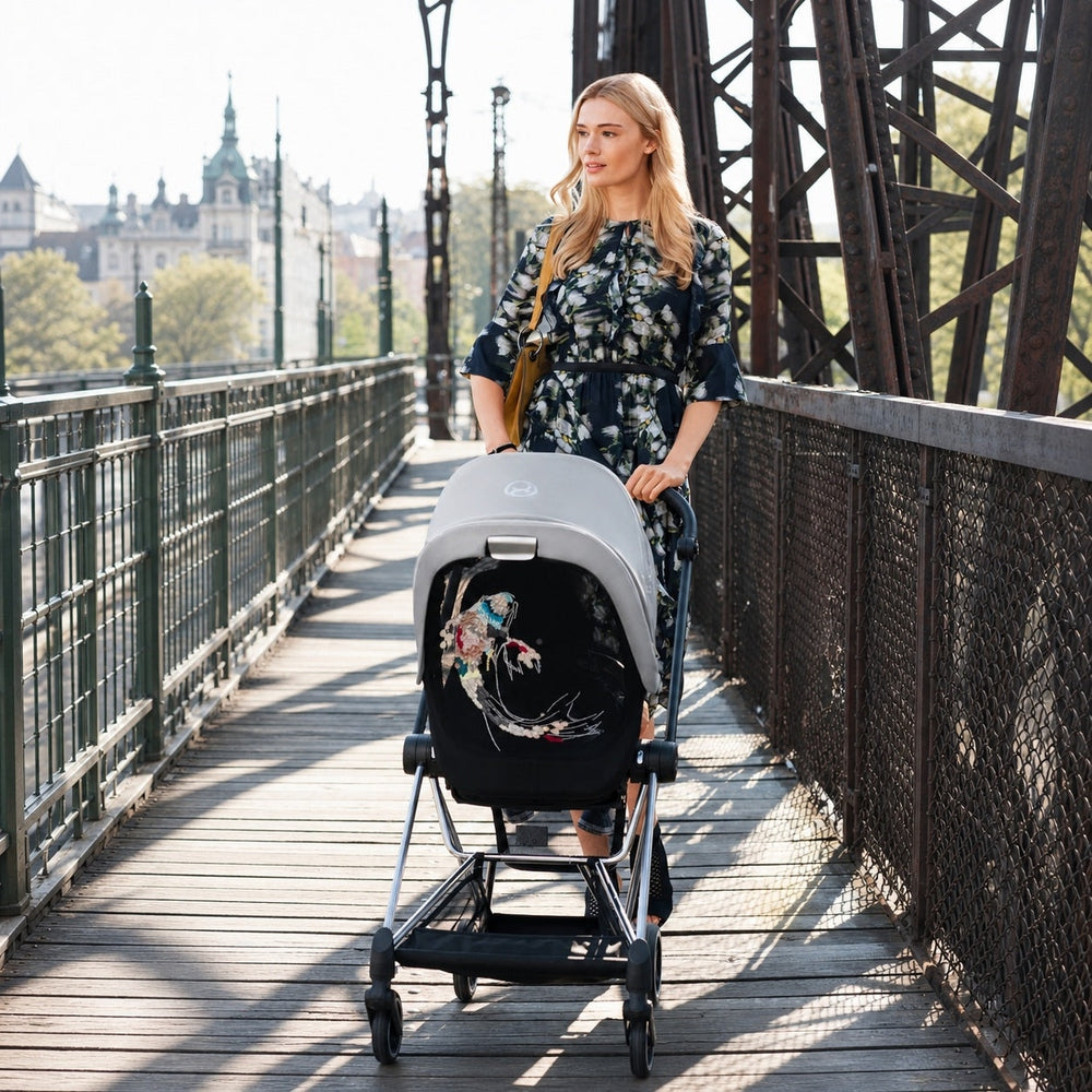 Lifestyle image of the Cybex Platinum Mios 3 Compact Stroller Limited Edition on a city bridge with a model pushing the stroller.