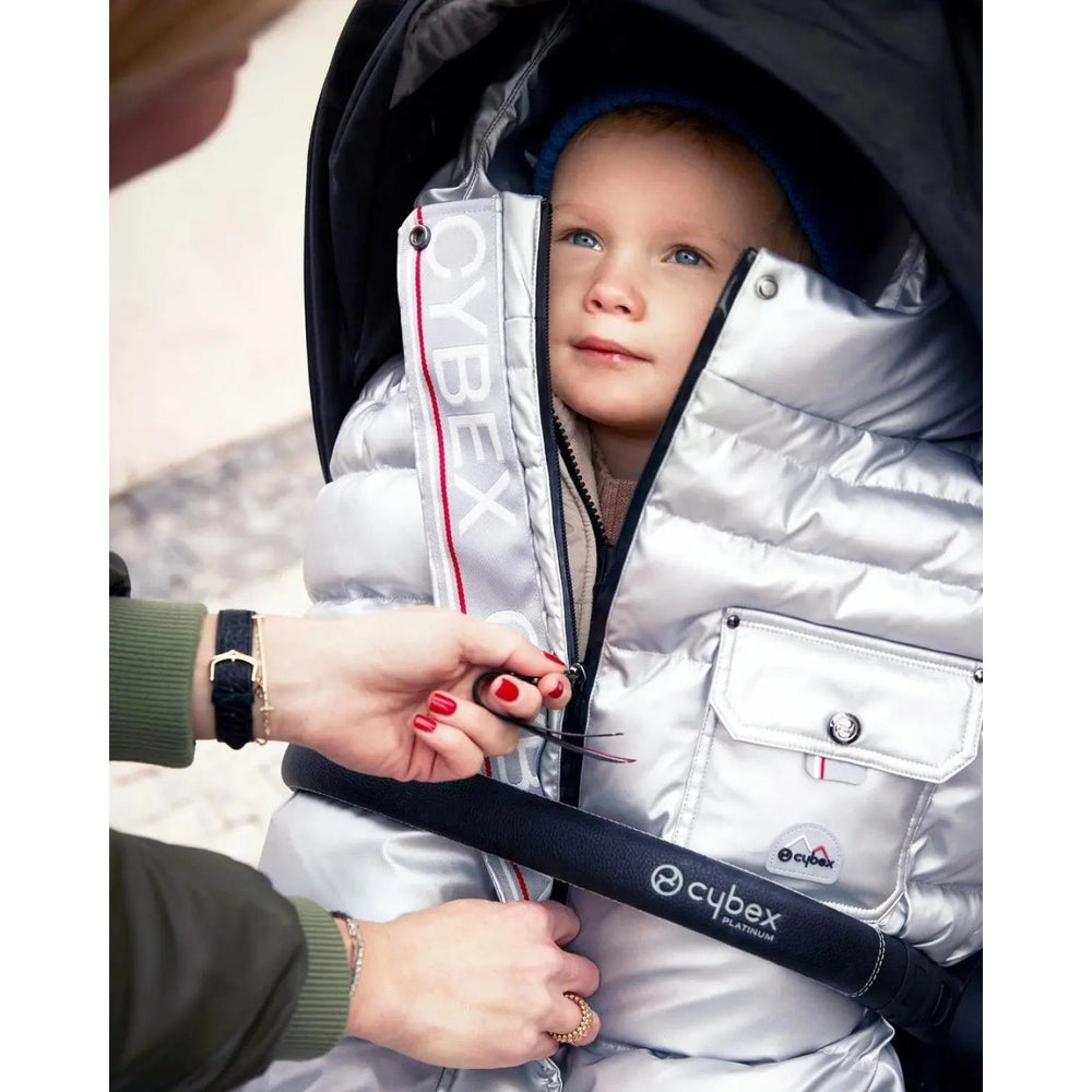 Close-up of the Cybex Winter Footmuff in silver metallic quilted fabric, zipper-secured on a stroller with a child inside.