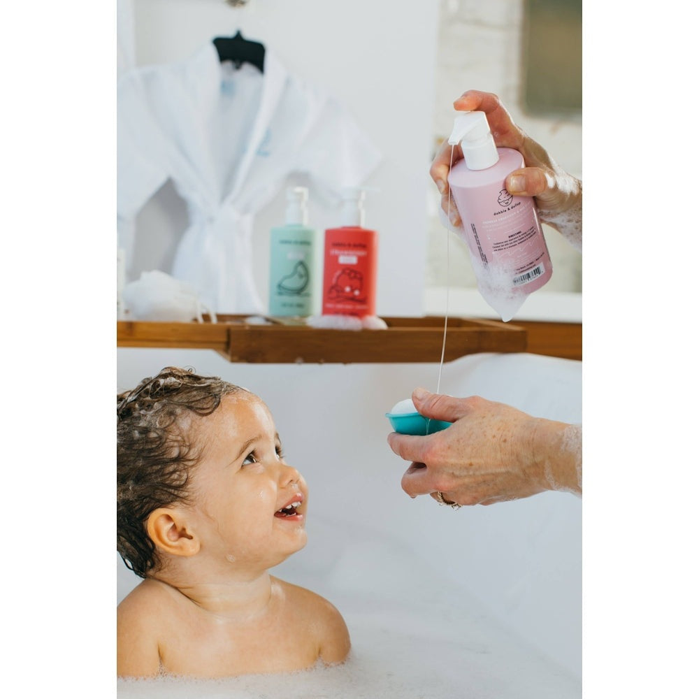 Dabble & Dollop All-Natural Shampoo, Body Wash & Bubbles Coconut being poured for a baby bath by a caregiver.