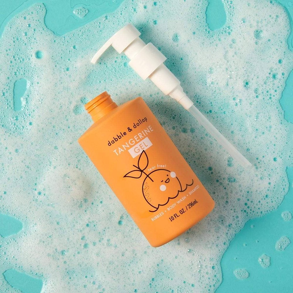 Dabble & Dollop All-Natural Tangerine shampoo and body wash bottle with white pump resting on turquoise soapy bubbles.
