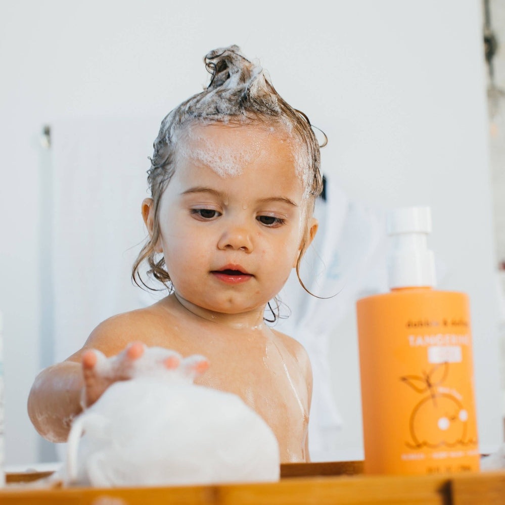 Dabble & Dollop All-Natural Shampoo, Body Wash & Bubbles Tangerine: toddler lathers foamy bubbles beside the orange pump bottle.