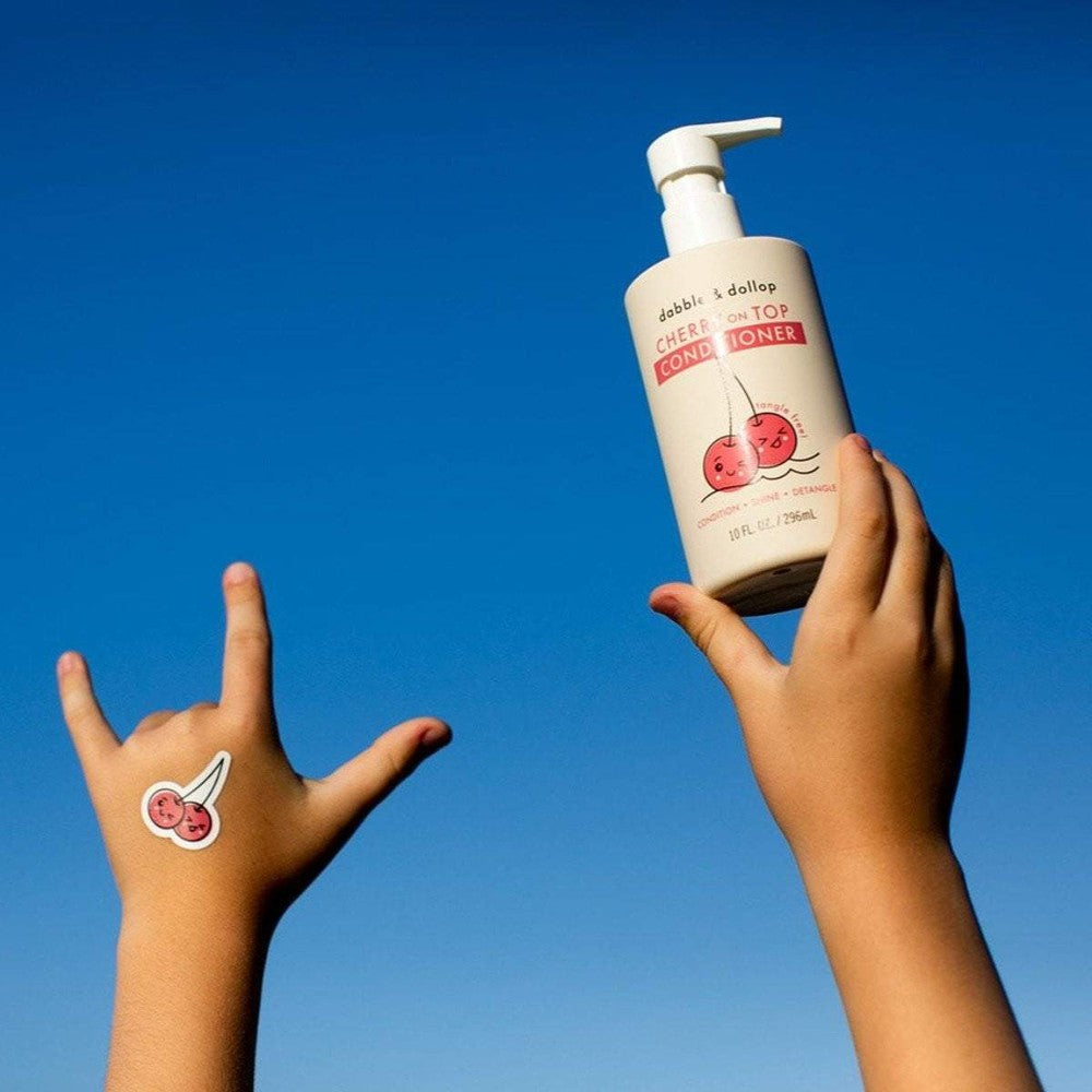 Dabble & Dollop Cherry on Top Conditioner bottle with pump held aloft by a hand against a bright blue sky.