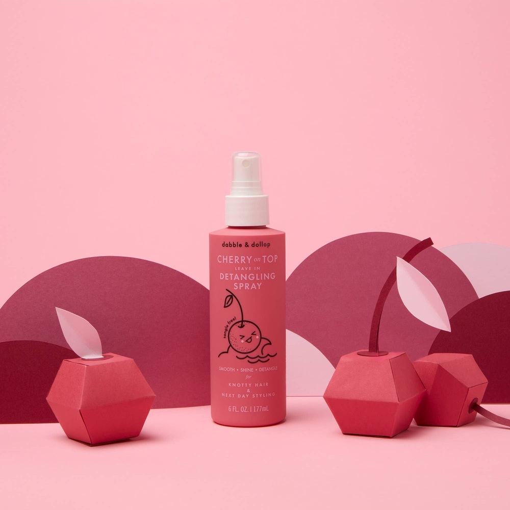 Dabble & Dollop Cherry on Top Detangling Spray bottle stands upright in a pink, cherry-themed scene.
