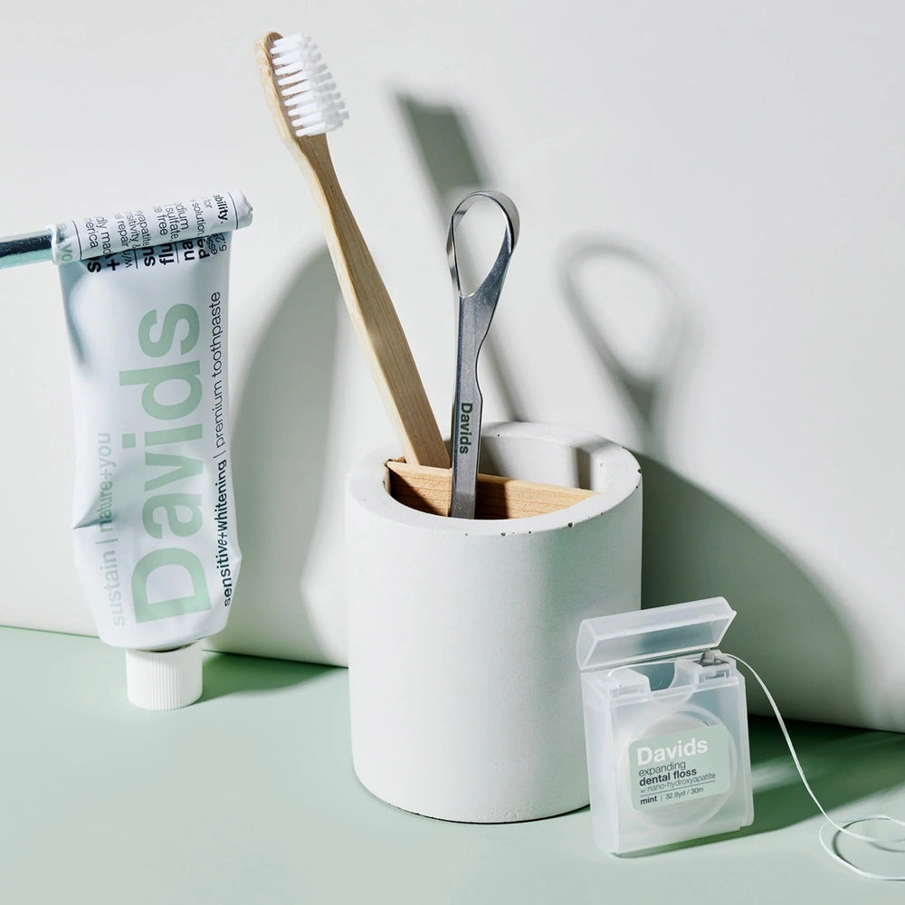 Davids toothpaste fluoride-free peppermint tube stands upright beside a wooden toothbrush and mint dental floss.