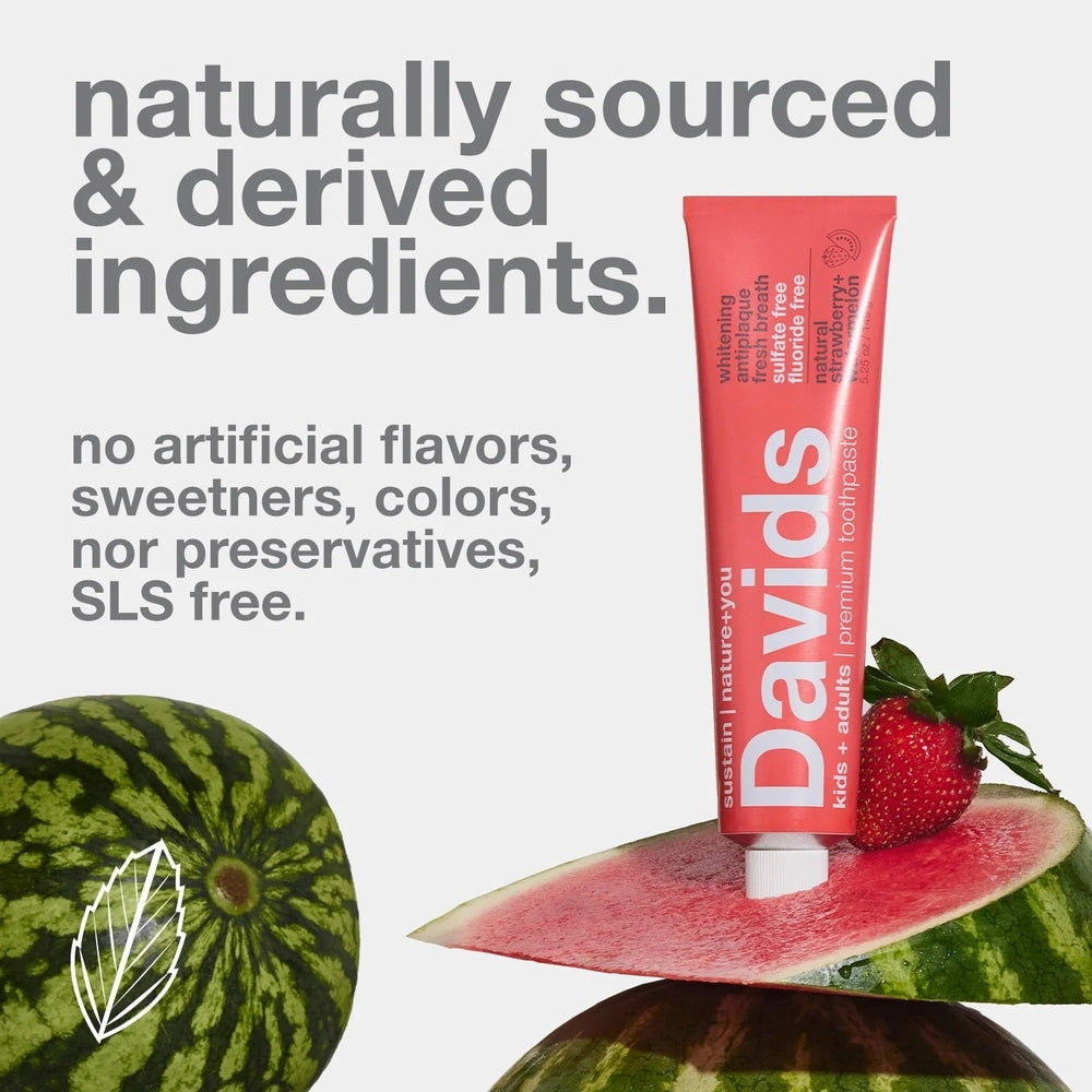 Davids Toothpaste Fluoride Free Strawberry Watermelon stands upright beside a watermelon slice and strawberry.
