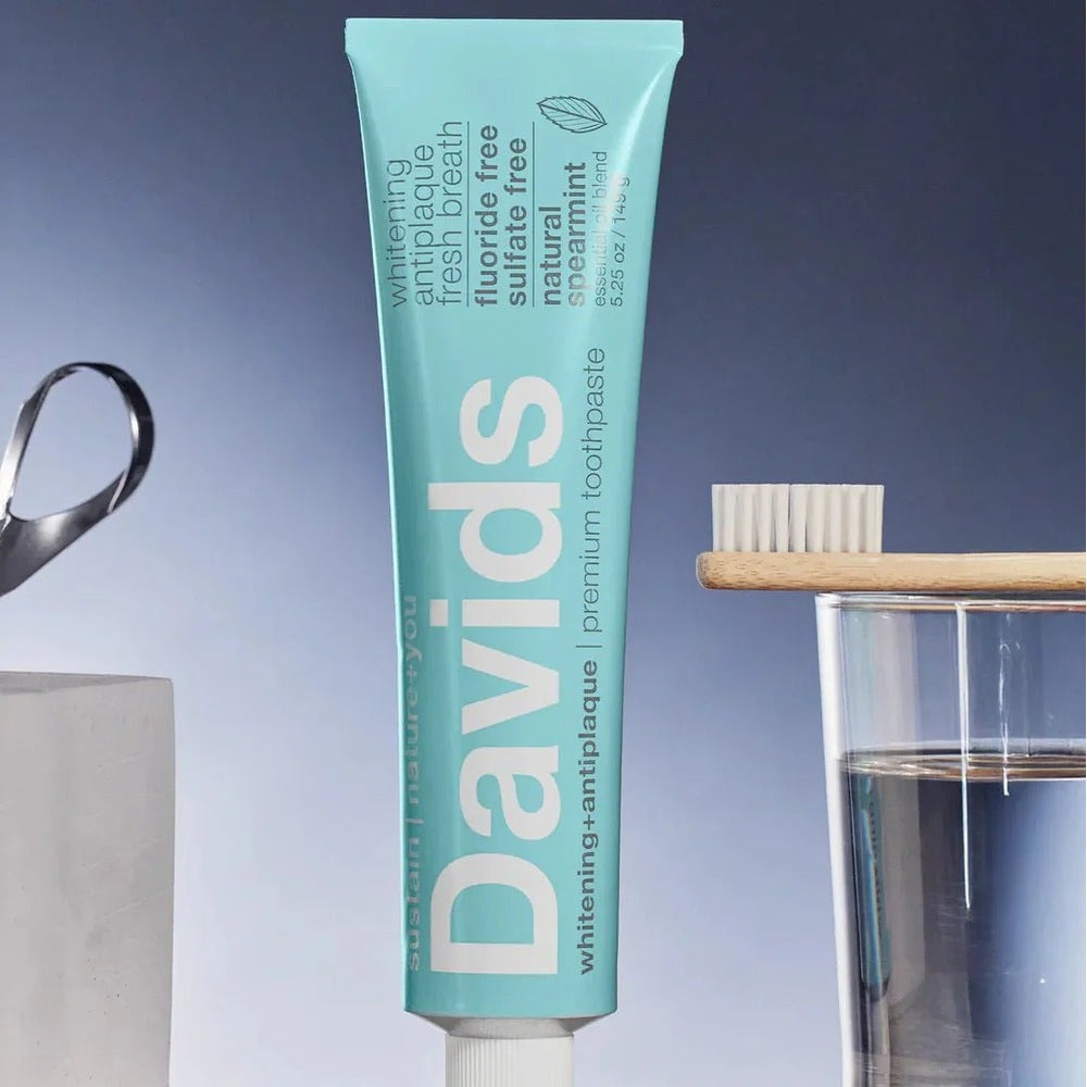 Davids toothpaste fluoride-free spearmint tube standing upright beside a toothbrush on a glass.