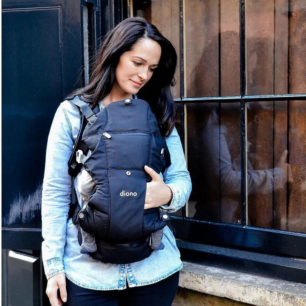 Diono Carus Essentials 3-in-1 baby carrier in black worn by a woman in a denim jacket, cradling a baby.
