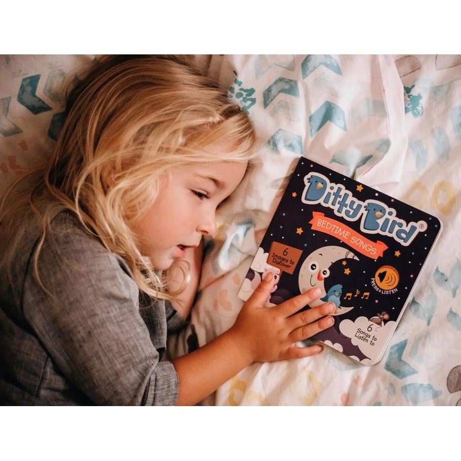 Ditty Bird Sound Book Bedtime Songs USB-C rechargeable; a young girl cuddles the illustrated book on a pastel bedspread.