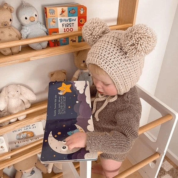 Ditty Bird Sound Book Bedtime Songs USB-C Rechargeable; toddler in beige knit hat reads the book beside plush toys.