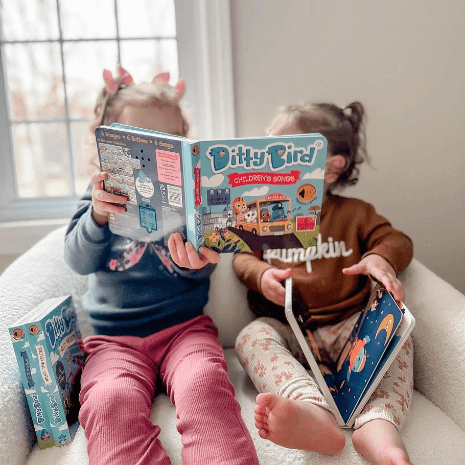 Ditty Bird Sound Book Children's Songs USB-C Rechargeable held by two kids reading on a cozy white sofa.