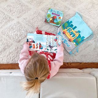Ditty Bird Sound Book Classical Ballet Music USB-C Rechargeable; a child sits and reads the illustrated book beside a blue Ditty Bird bag.