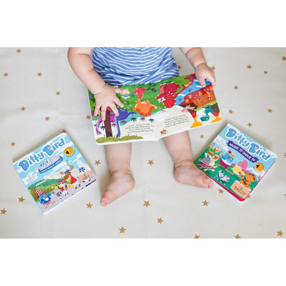 Ditty Bird Dinosaur Sounds USB-C rechargeable sound book; baby sits and holds the colorful story amid two Ditty Bird boxes.
