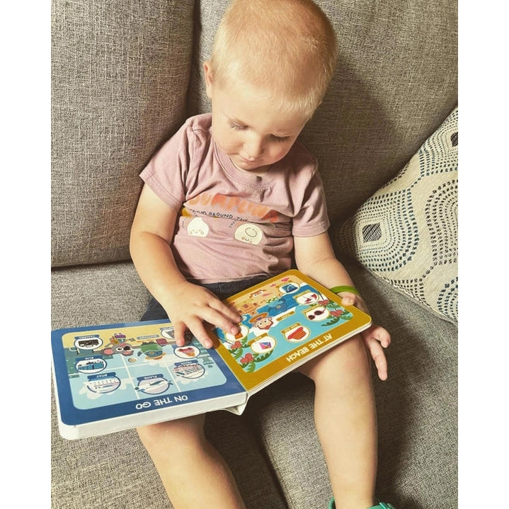 Ditty Bird Sound Book First 100 Places USB-C Rechargeable educational toy; toddler on a sofa flips colorful pages.