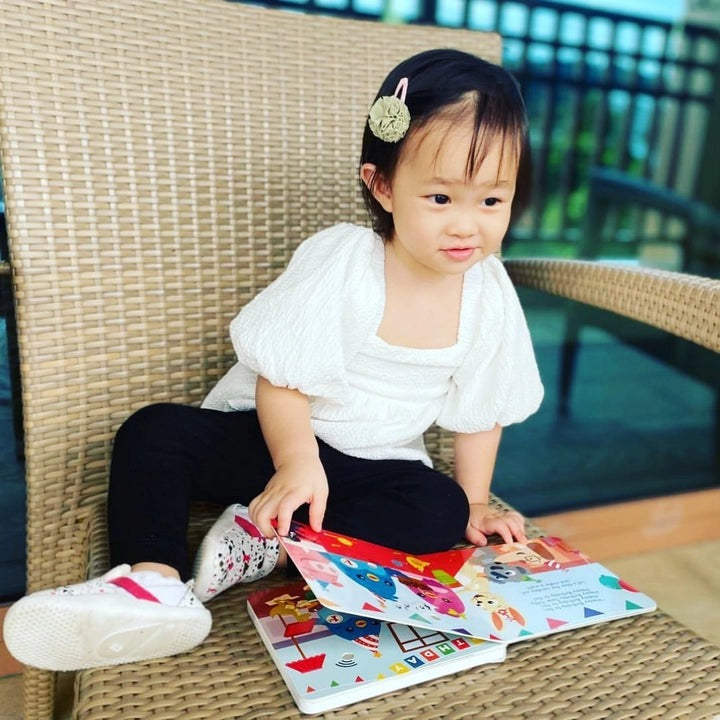 Ditty Bird Sound Book Happy Birthday USB-C Rechargeable being explored by a toddler flipping colorful pages on a wicker chair.