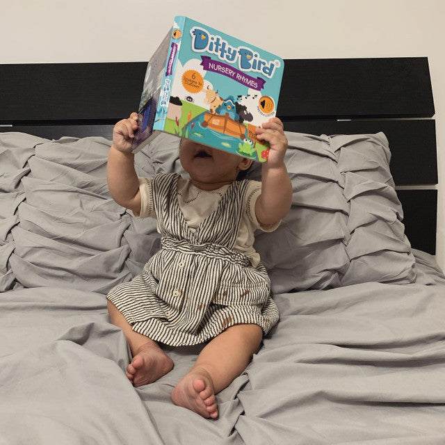 Ditty Bird Sound Book Nursery Rhymes USB-C Rechargeable; a baby sits on a bed holding it.