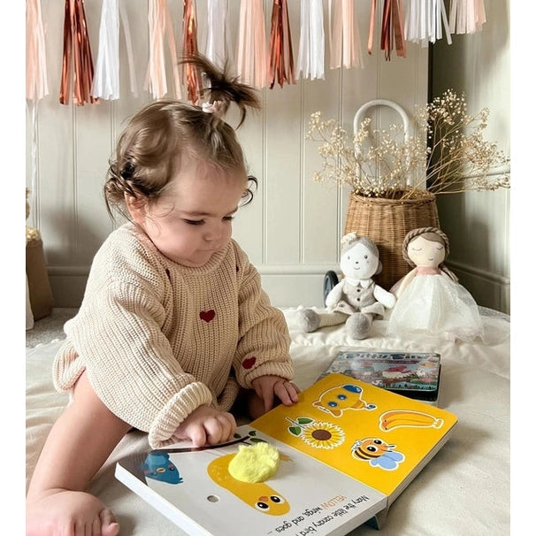 Ditty Bird Sound Book Touch the Colors USB-C Rechargeable; toddler taps bright pages, exploring colors in a cozy playroom.