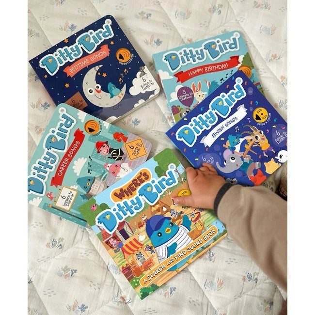Ditty Bird Sound Book Where's Ditty Bird USB-C Rechargeable, a colorful educational book set on a bed with a child's hand reaching for one.