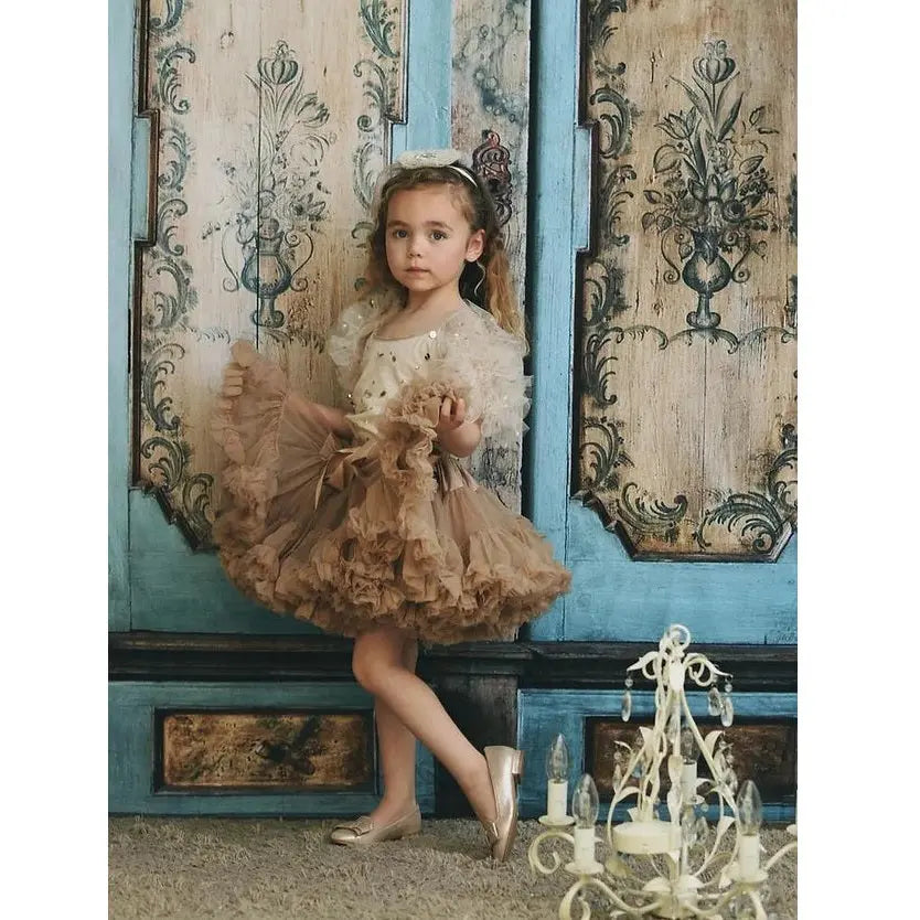 Dolly by Le Petit Tom Pettiskirt Little Mermaid Cookie Taupe, a girl in a layered taupe tutu posing by blue ornate doors.