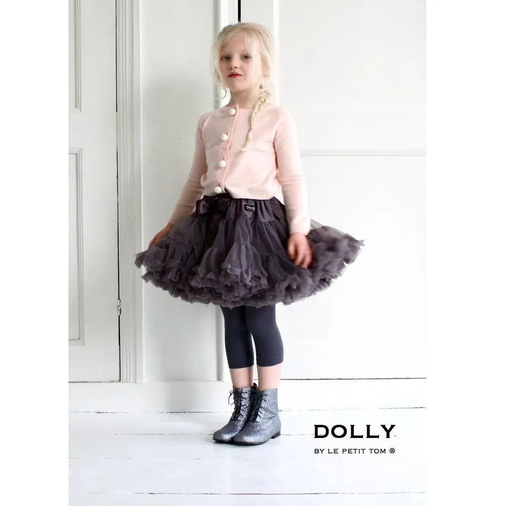 Dolly by Le Petit Tom Pettiskirt Princess & The Pea in dark grey tulle as a girl twirls in a pink cardigan and glitter boots.