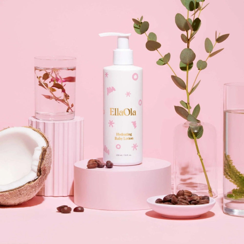 EllaOla Fragrance Free Hydrating Baby Lotion 230ml on pink pedestal with pump, greenery and coconut.