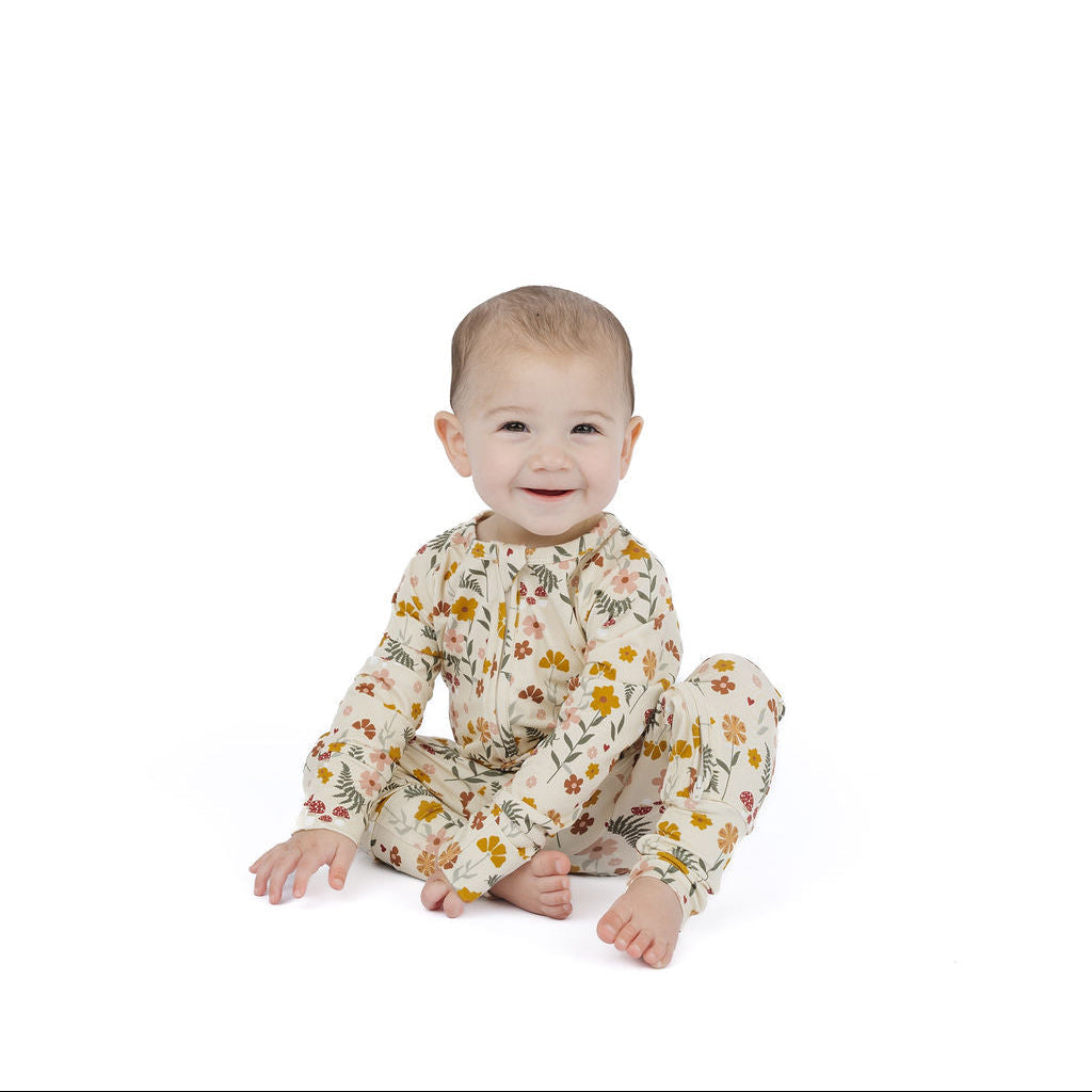 Toadstool Garden Bamboo Convertible Footie Romper Beige And Multi – a baby sitting on a white studio background wearing a cream-colored long-sleeve footless onesie with a yellow and orange floral pattern