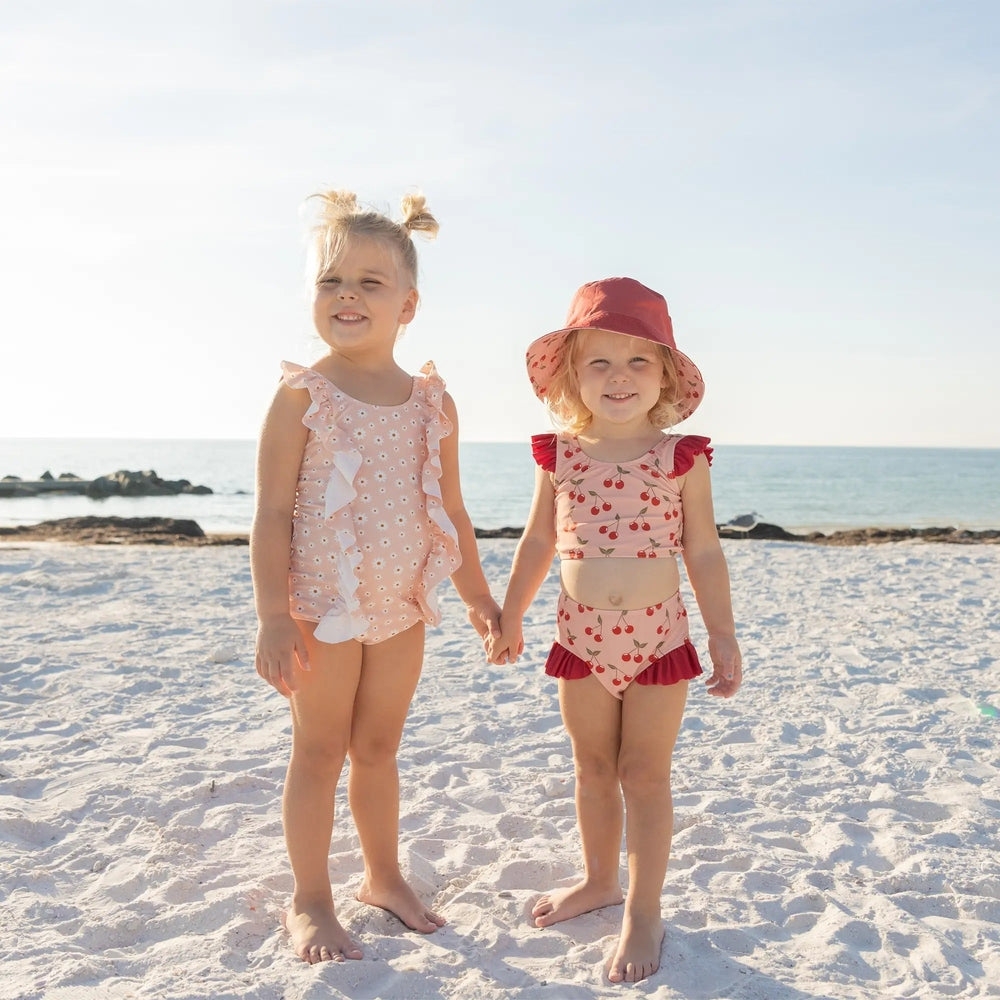 Two young girls in swimsuits standing on a sandy beach with ocean in the background.