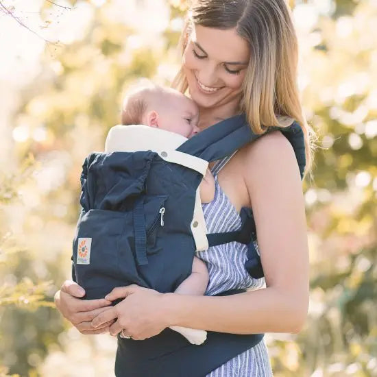 ERGOBABY Easy Snug Infant Insert in navy with cream straps worn by a smiling mother outdoors with baby.