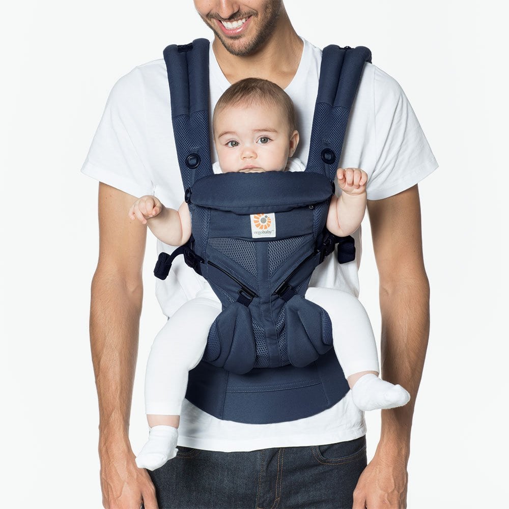 Ergobaby Omni 360 Cool Air Mesh navy baby carrier worn by parent, baby securely seated facing inward.
