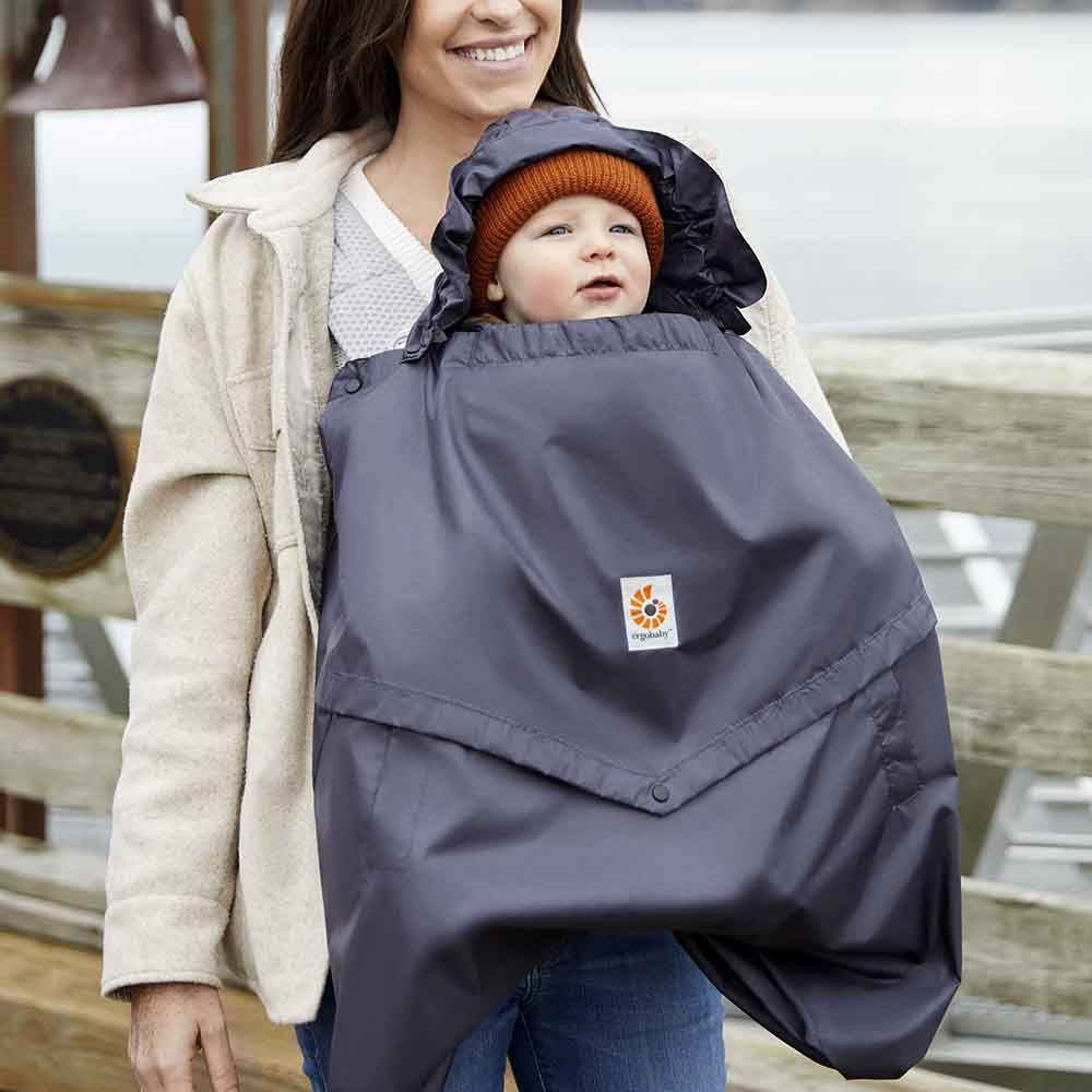 Ergobaby rain and wind carrier cover in charcoal; baby in orange knit hat snug inside.