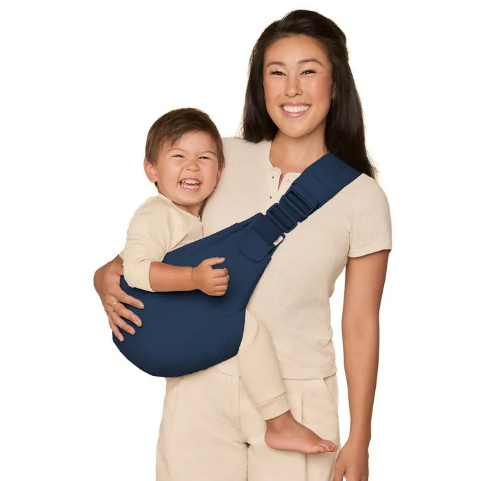 Smiling mom wears a blue Ergobaby Upsie Sling Carrier with baby secured high on her chest.