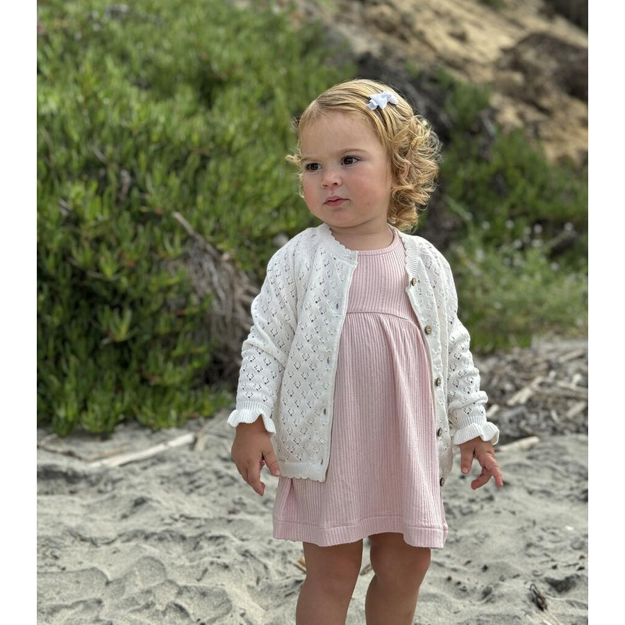 Ettie & H Aurora Cardigan White worn by a toddler on a sandy beach, white knit cardigan with buttons over a pink dress.