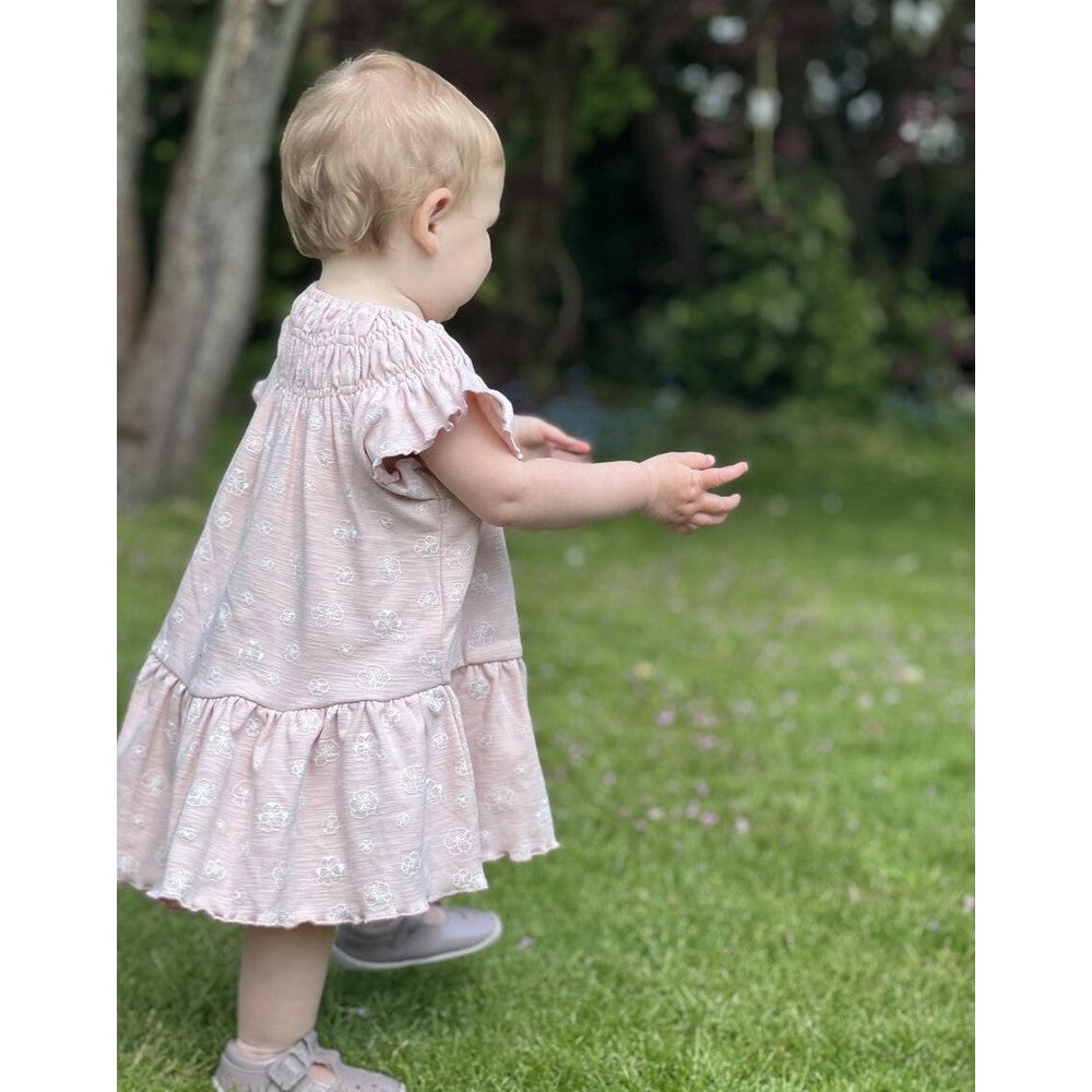 Ettie & H Pale Pink Flowers Dress on a toddler walking on grass, pink floral print with ruffled sleeves.