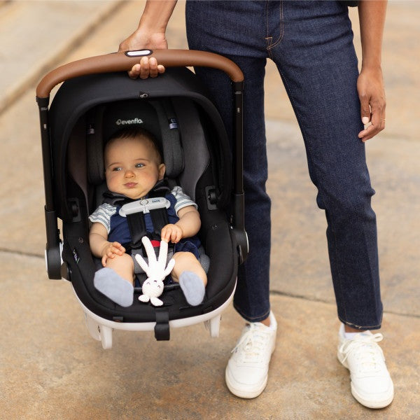 Evenflo Gold Shyft Dualride infant car seat and stroller combo; black seat with brown carry handle, baby seated.
