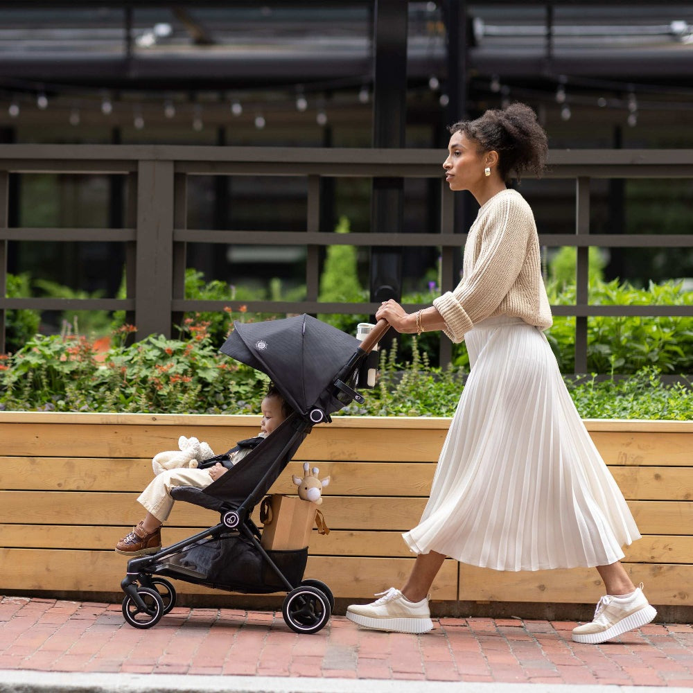 Evenflo Hummingbird ultralight carbon fiber stroller; black frame with child seated, mom pushing on sidewalk