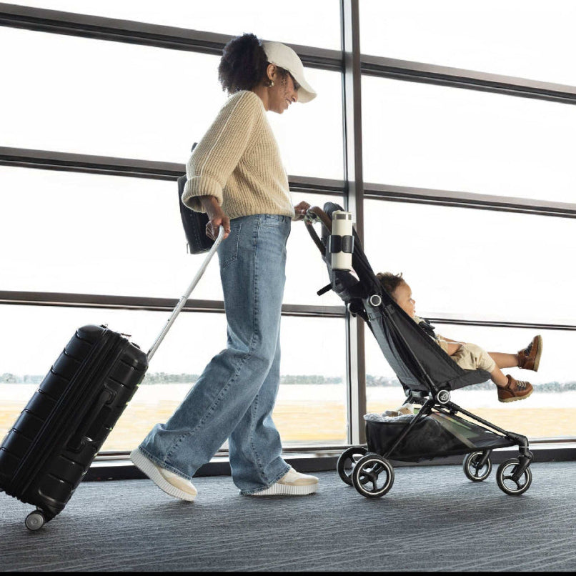Evenflo Hummingbird Ultra-Lightweight carbon fiber stroller; black frame with child seated, parent pulling rolling suitcase