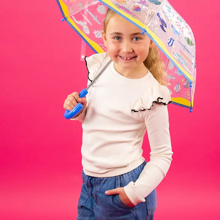 Floss and Rock Ocean Colour Changing Transparent Umbrella held by a smiling girl on a pink background.