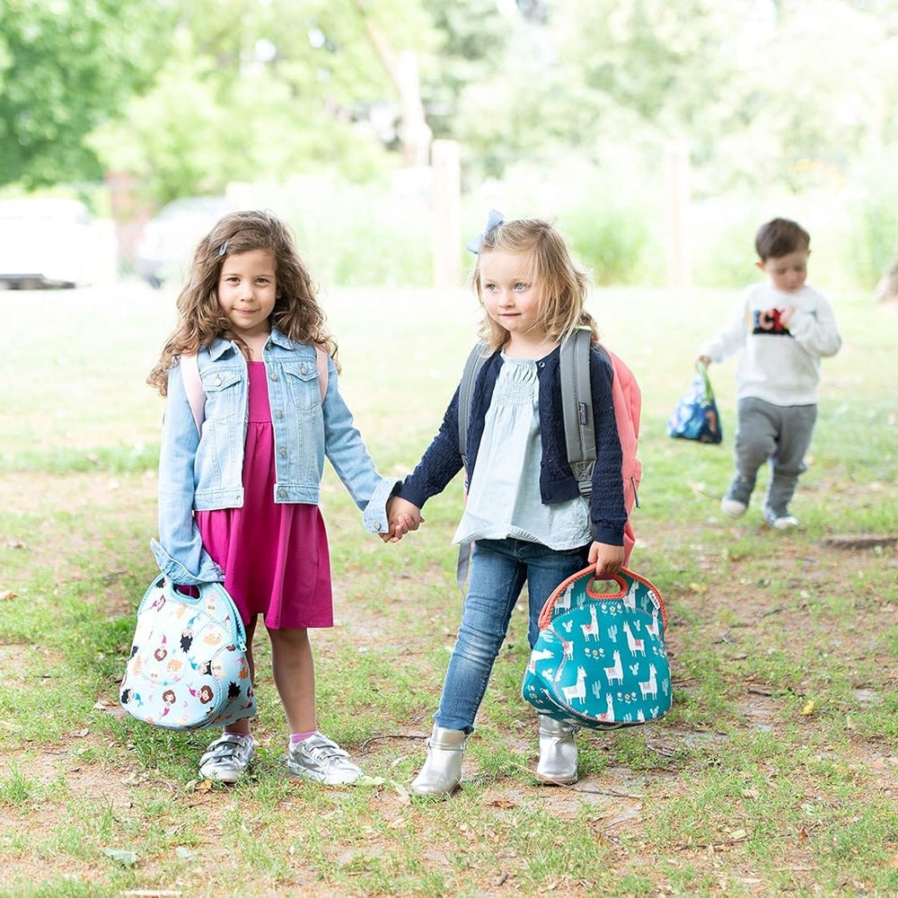 Two kids in a park carry insulated lunch bags; one light-blue mermaid print, the other teal with white animals.