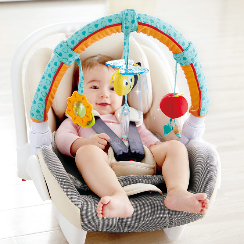 Hape Garden Friends Play Arch over baby car seat with teal-orange frame and hanging sun, bee, apple toys
