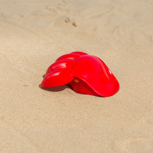 Hape Power Paw Red toy on sandy beach; bright red plastic outdoor play accessory