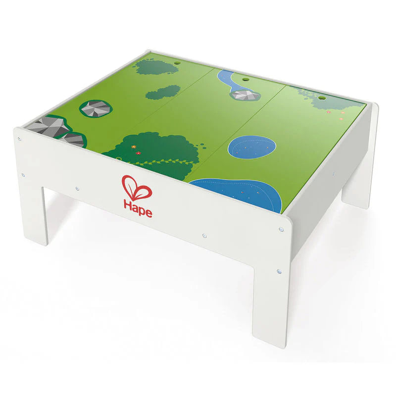 Hape Reversible Train & Storage Table, white frame with a green landscape top; kids push trains on the reversible surface.