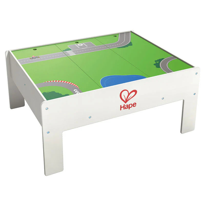 Hape Reversible Train & Storage Table in white wood with a green train-track surface showing trains on the track.