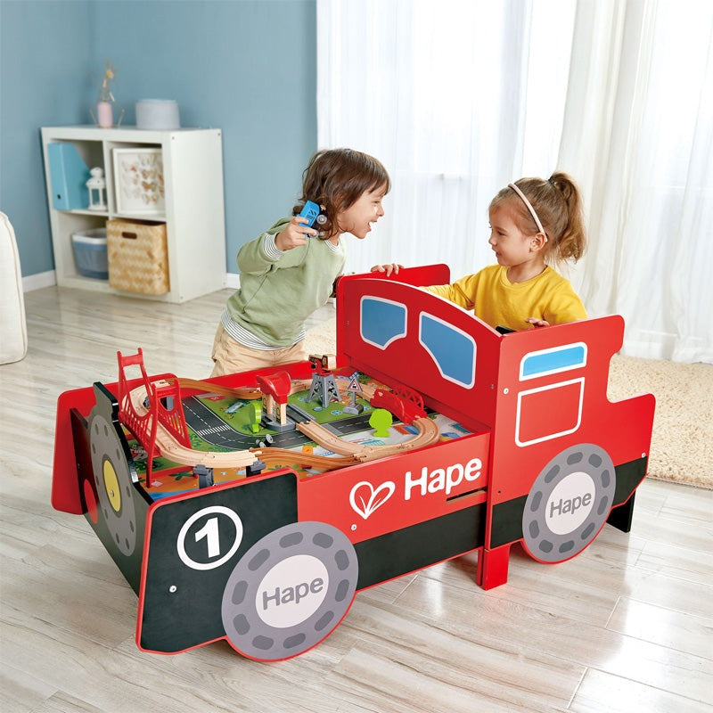 Hape Ride-On Engine Table red train car design with two kids playing on a wooden train track setup