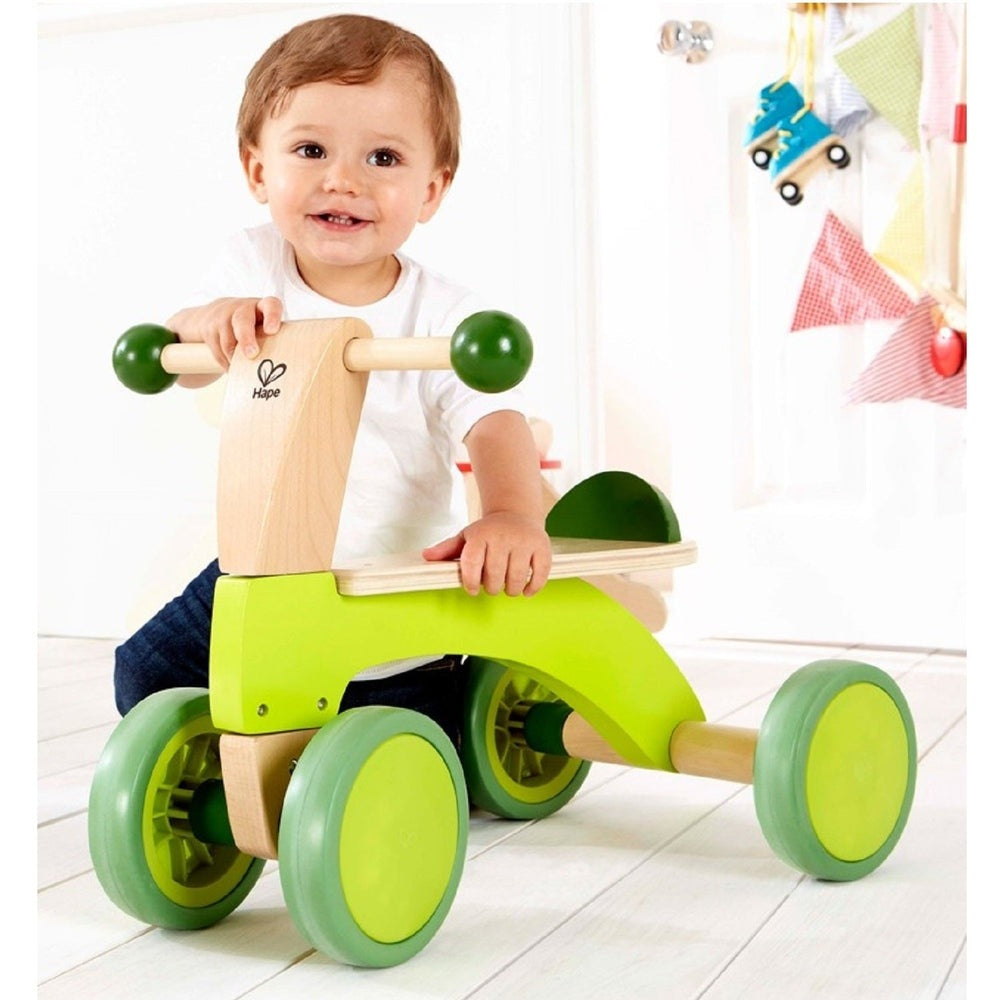 Hape Scoot Around wooden toddler scooter in lime-green with green wheels; child rides and smiles.