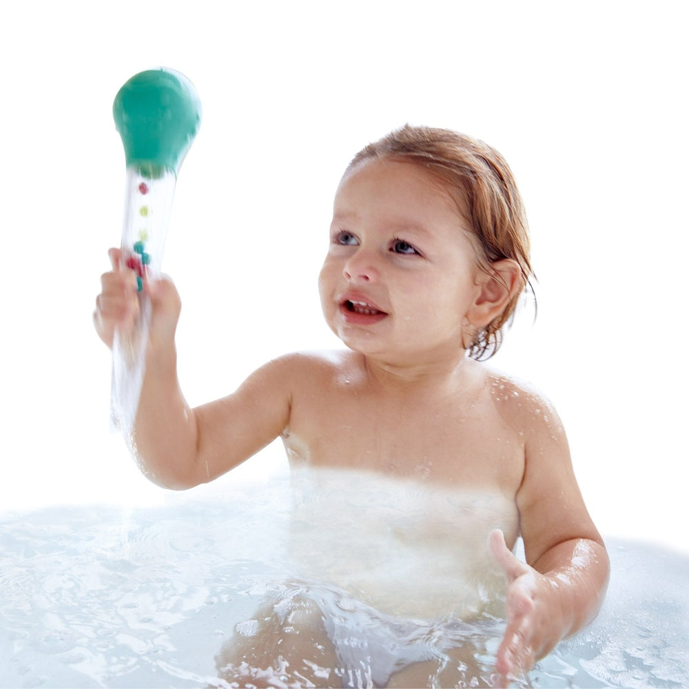 Hape Squeeze & Squirt bath toy, clear tube with colorful beads and green cap, held by toddler