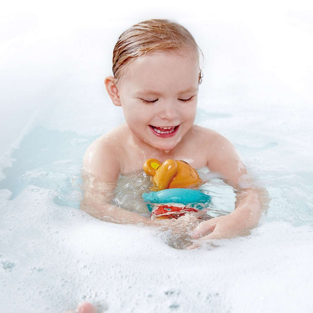 Hape Swimmer Teddy Wind-Up Toy; yellow teddy on blue base, baby smiling in bath.