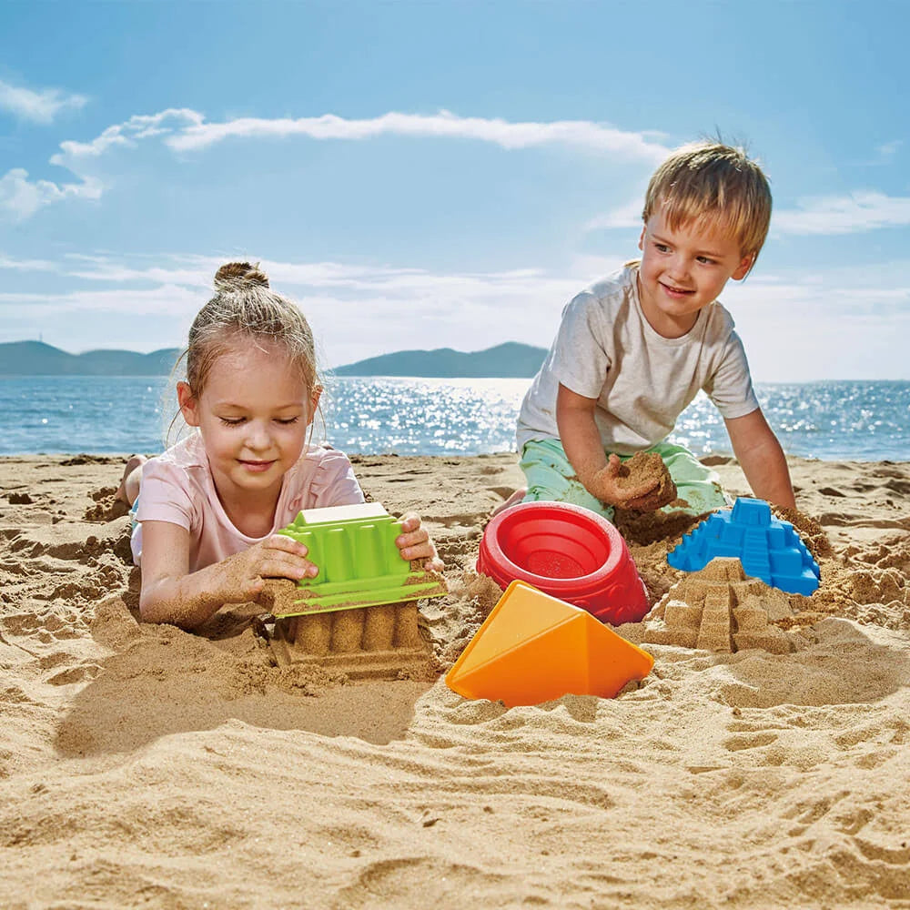 Hape Parthenon sand mold toys; two children playing on a sunny beach with colorful plastic molds.