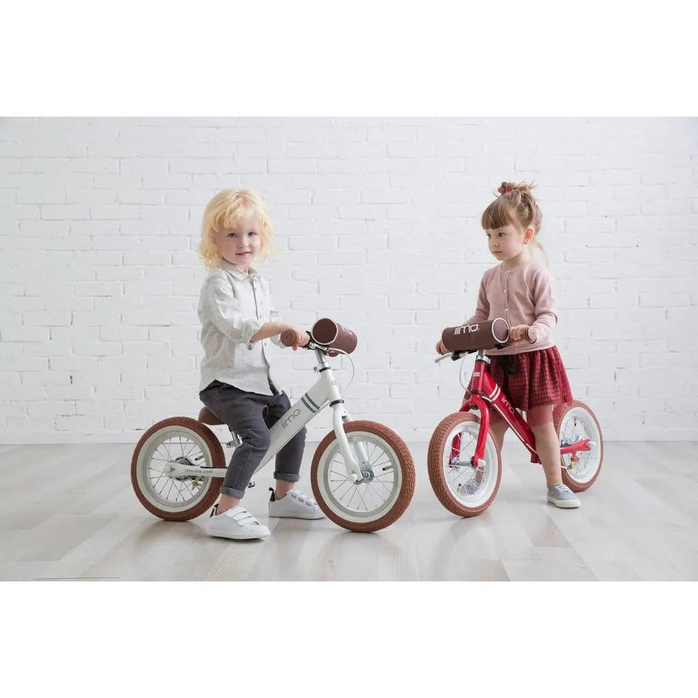 Iimo Balance Bike; two kids ride indoors on white and red frames with brown tires.